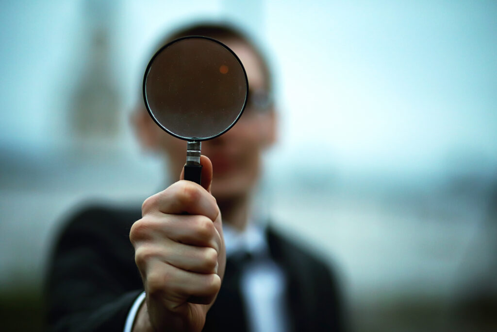 A man holding a magnifying glass symbolizing identifying customer needs.